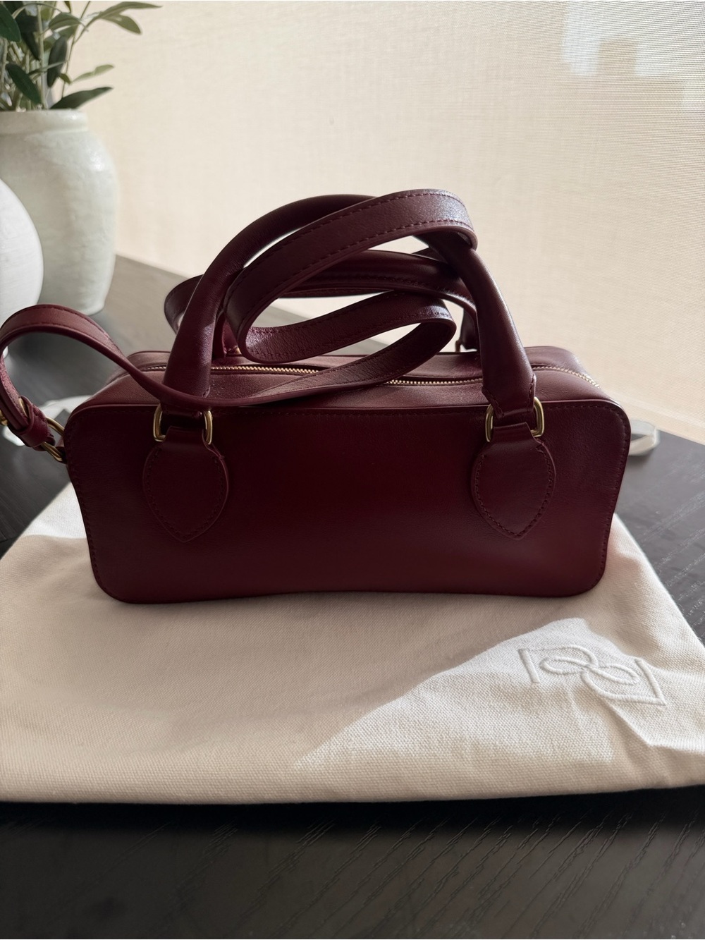 Reformation leather burgundy bag with top handle and long strap.